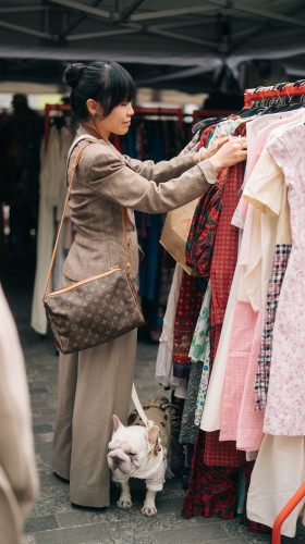 Person looks through clothes rail with dog at feet