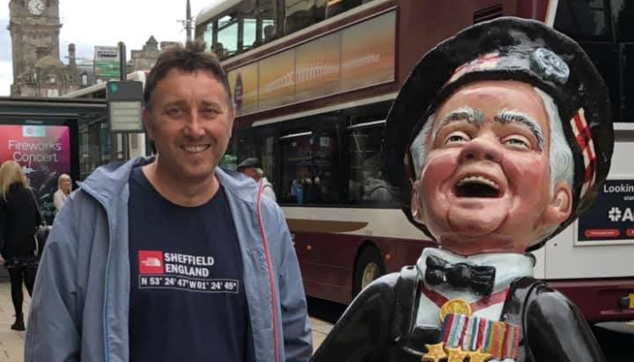 Picture of a man on a high street posing next to a character statue