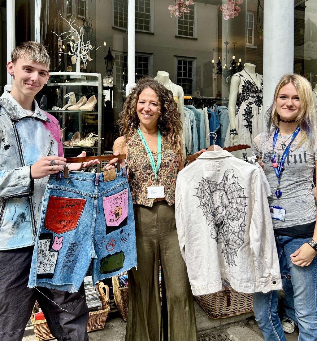Staff and students pose with denim fashion creations outside store.