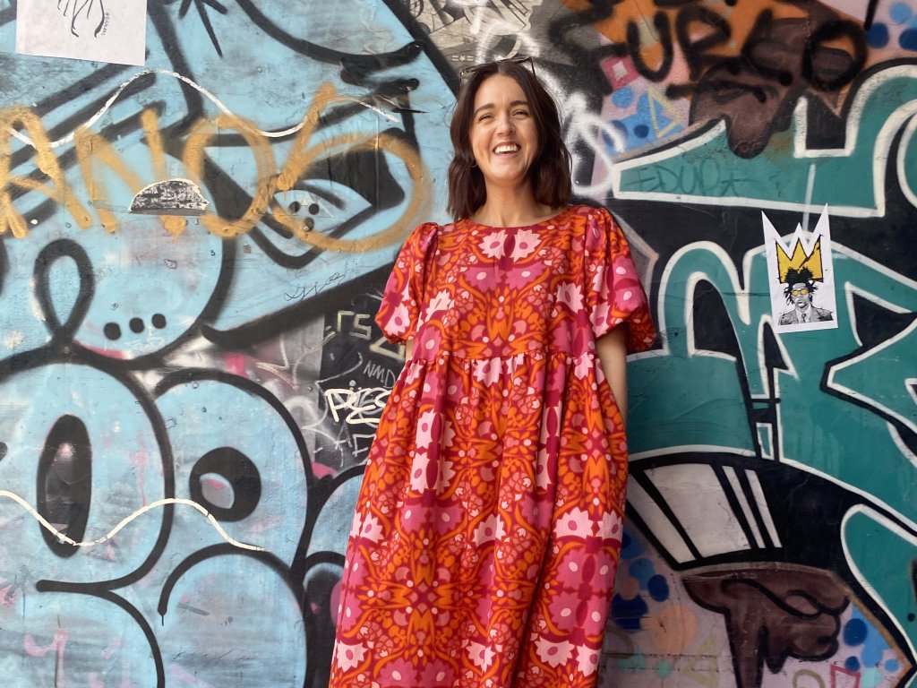Model in bright dress poses in front of graffiti wall.