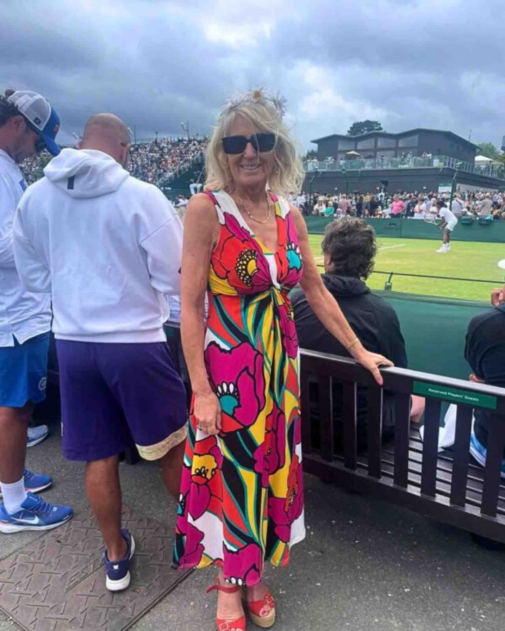 Brightly dressed woman beside a tennis court.